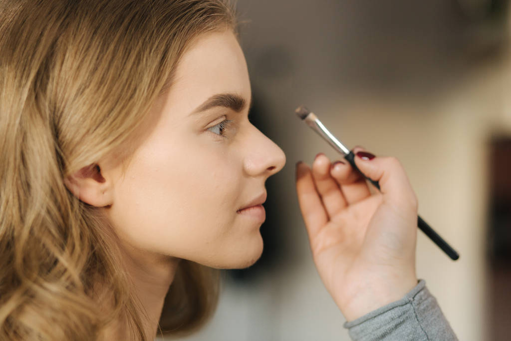 Makeup artist work in her beauty studio. Portrait of Woman applying by professional make up master. Beautiful make up artist start making a makeup for blond hair model